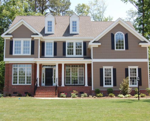 tan two story home with brick accents against a green lawn